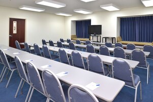 A conference room with rows of tables and chairs, a large screen, and a sofa.
