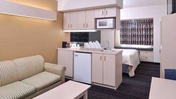 A compact hotel room with a kitchenette, a sofa, a small table, and a bed.