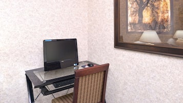 Escritorio de vidrio con una computadora portátil, una silla y un cuadro en la pared.