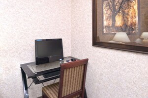 Escritorio de vidrio con una computadora portátil, una silla y un cuadro en la pared.