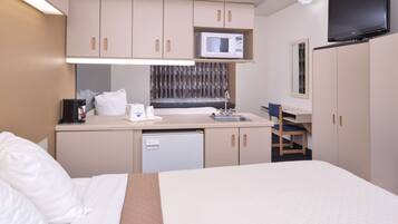 A compact hotel room with a bed, a kitchenette with a microwave, a sink, and a small seating area.