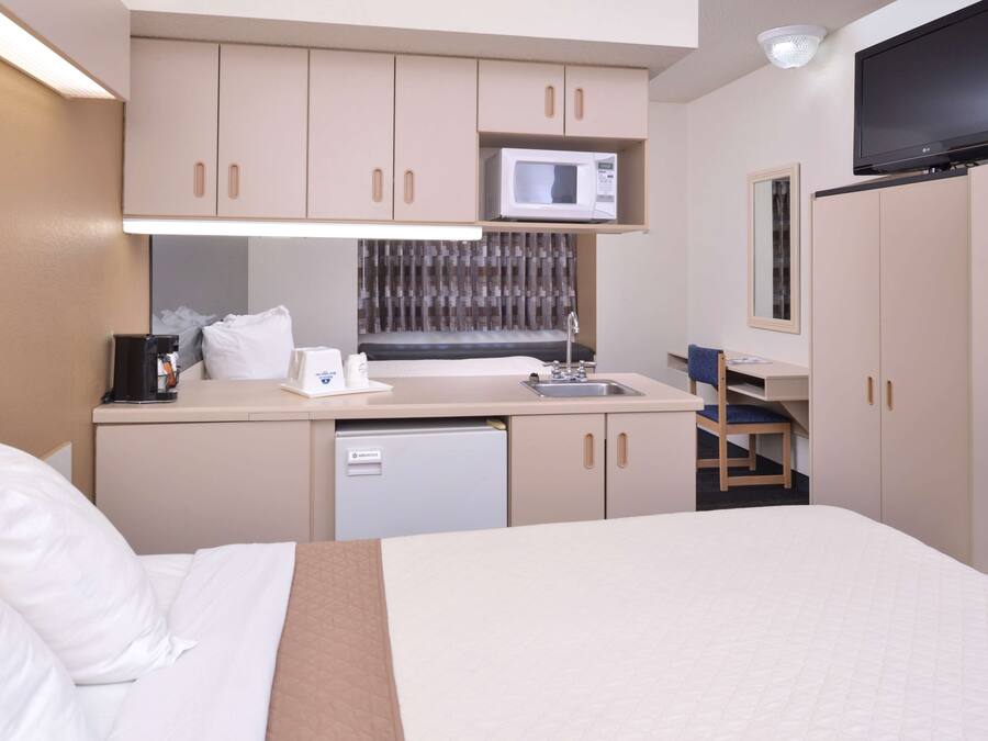 A compact hotel room with a bed, a kitchenette with a microwave, a sink, and a small seating area.