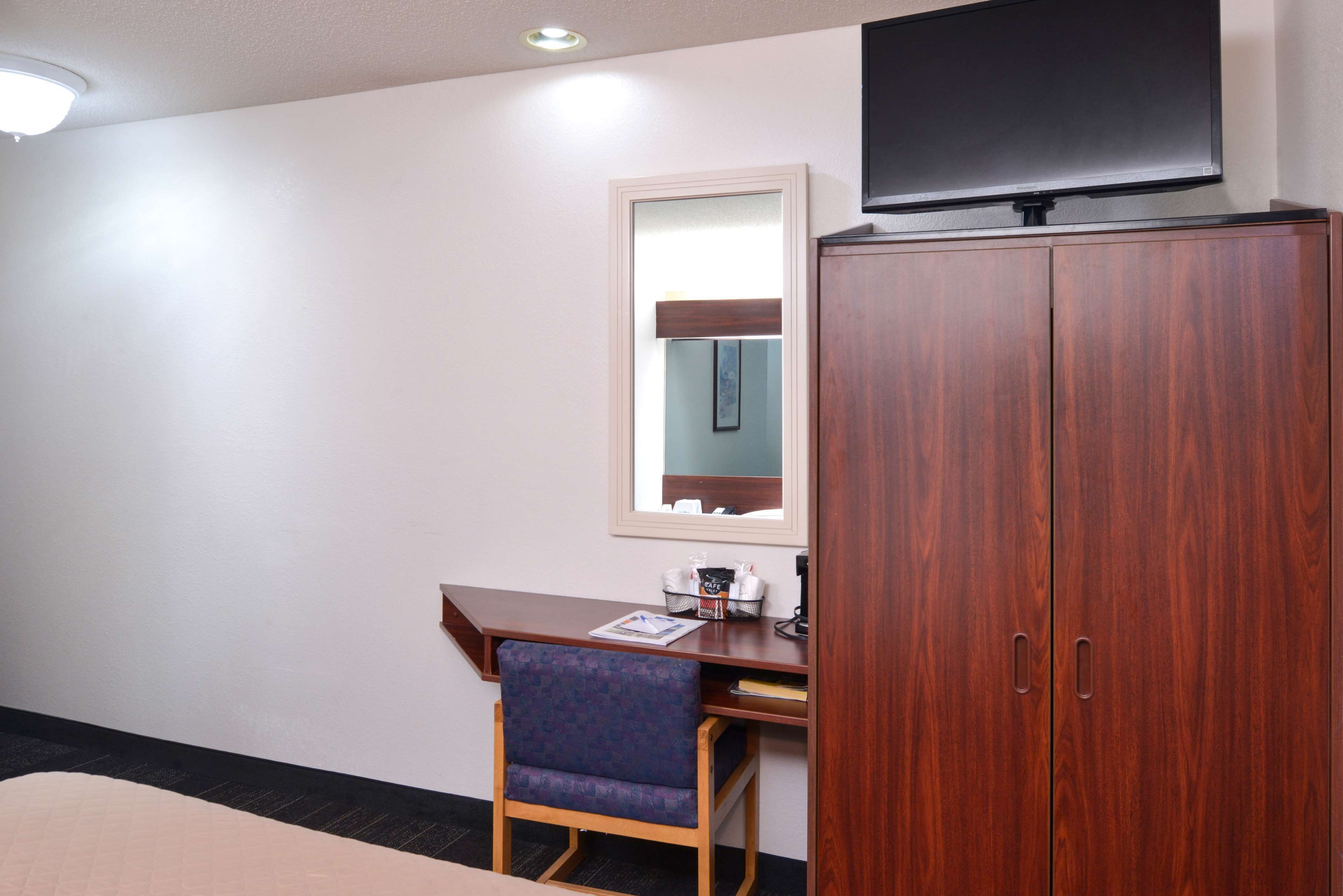 A hotel room with a wooden desk, a chair, a television mounted above the desk, and a wardrobe.