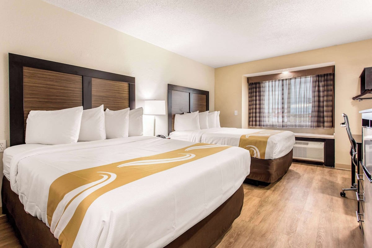 A hotel room with two beds, a large window with curtains, a TV, and a desk with a lamp.