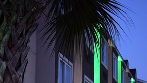 Un edificio de varios pisos con detalles de iluminación verde vertical y ventanas de marco blanco.
