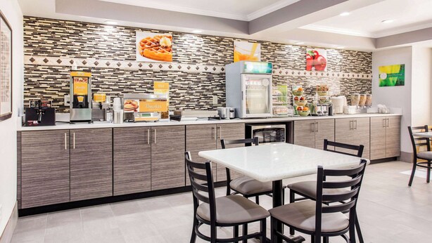 Una cocina moderna con encimera blanca, armarios de madera oscura y salpicadero de azulejos. Se ven dos sillas y una mesa en primer plano.