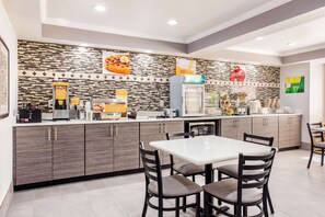A modern kitchen with a white countertop, dark wooden cabinets, and a tiled backsplash. There are two chairs and a table in the foreground.