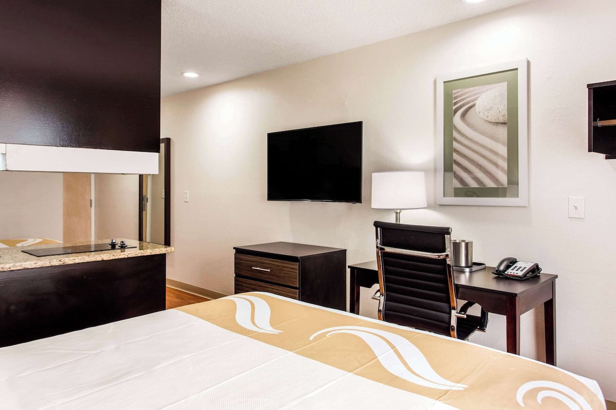 A hotel room with a bed, a desk, a chair, a television, a telephone, and a painting on the wall.