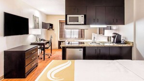 Una habitación de hotel compacta con kitchenette, una cama, un escritorio y un televisor.