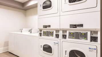 A laundry facility with multiple washing machines and dryers, including a control panel with digital displays.