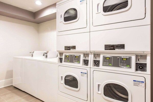 Un cuarto de lavandería con varias lavadoras y secadoras, incluyendo un panel de control con pantallas digitales.