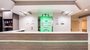 Un mostrador de recepción con un letrero verde que dice "QUALITY INN & SUITES" y un reloj encima.