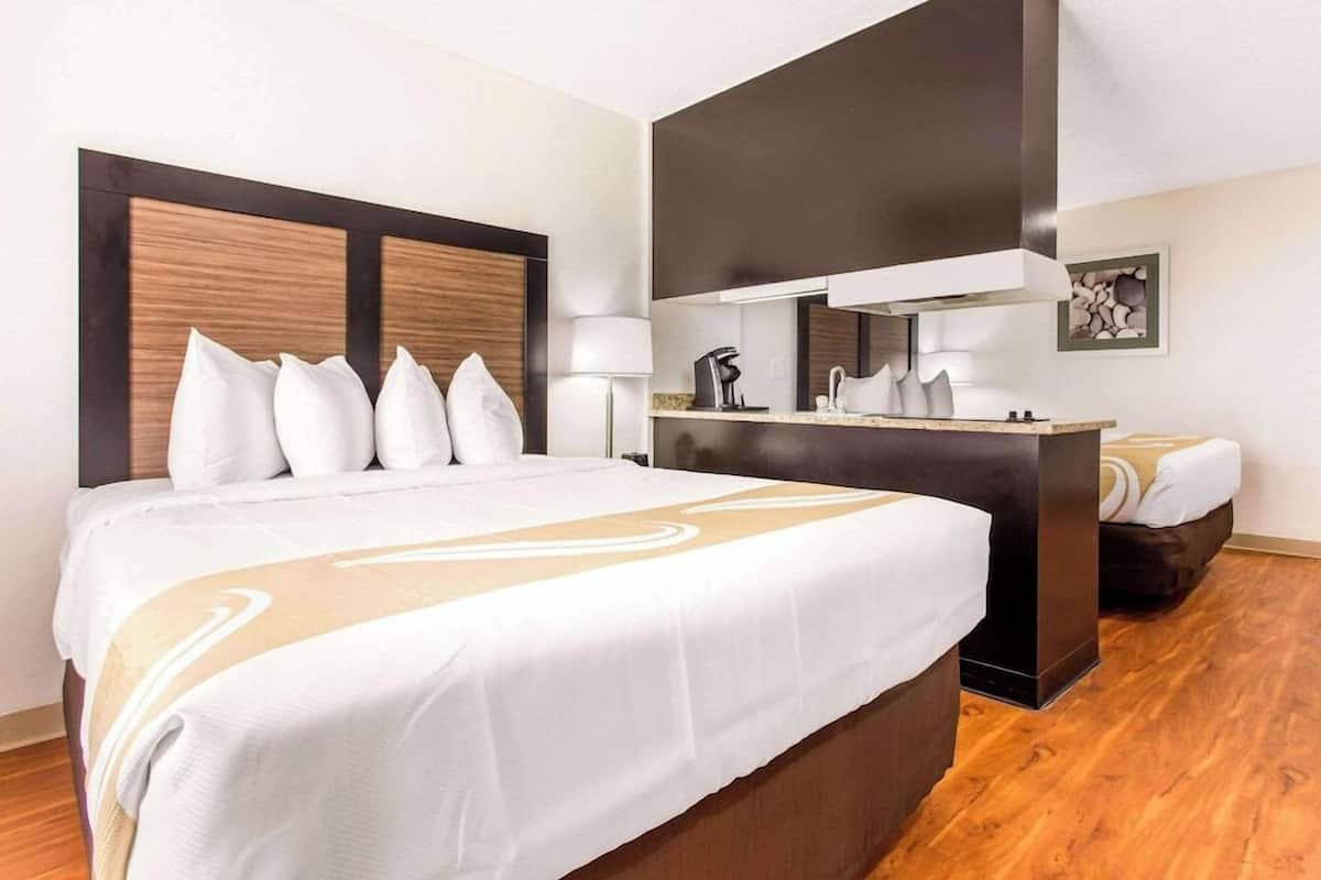 A hotel room with a large bed, a desk, a chair, a lamp, and a mirror.