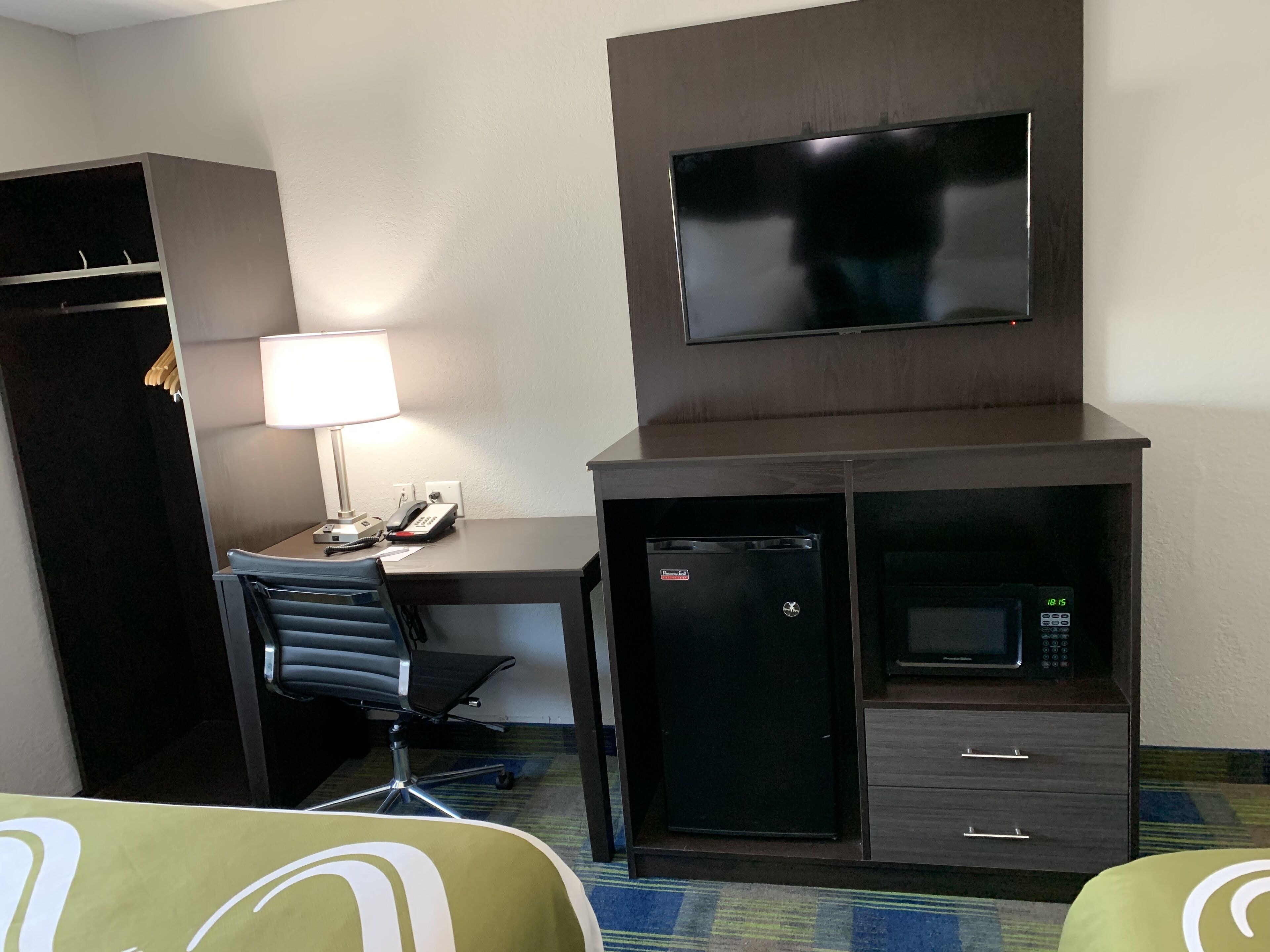A hotel room with a desk, chair, TV, mini-fridge, microwave, and a wardrobe.