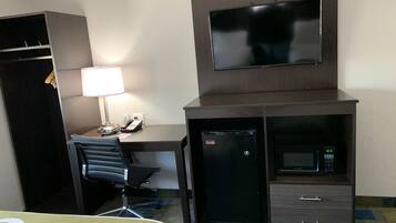 A hotel room with a desk, chair, TV, mini-fridge, microwave, and a wardrobe.