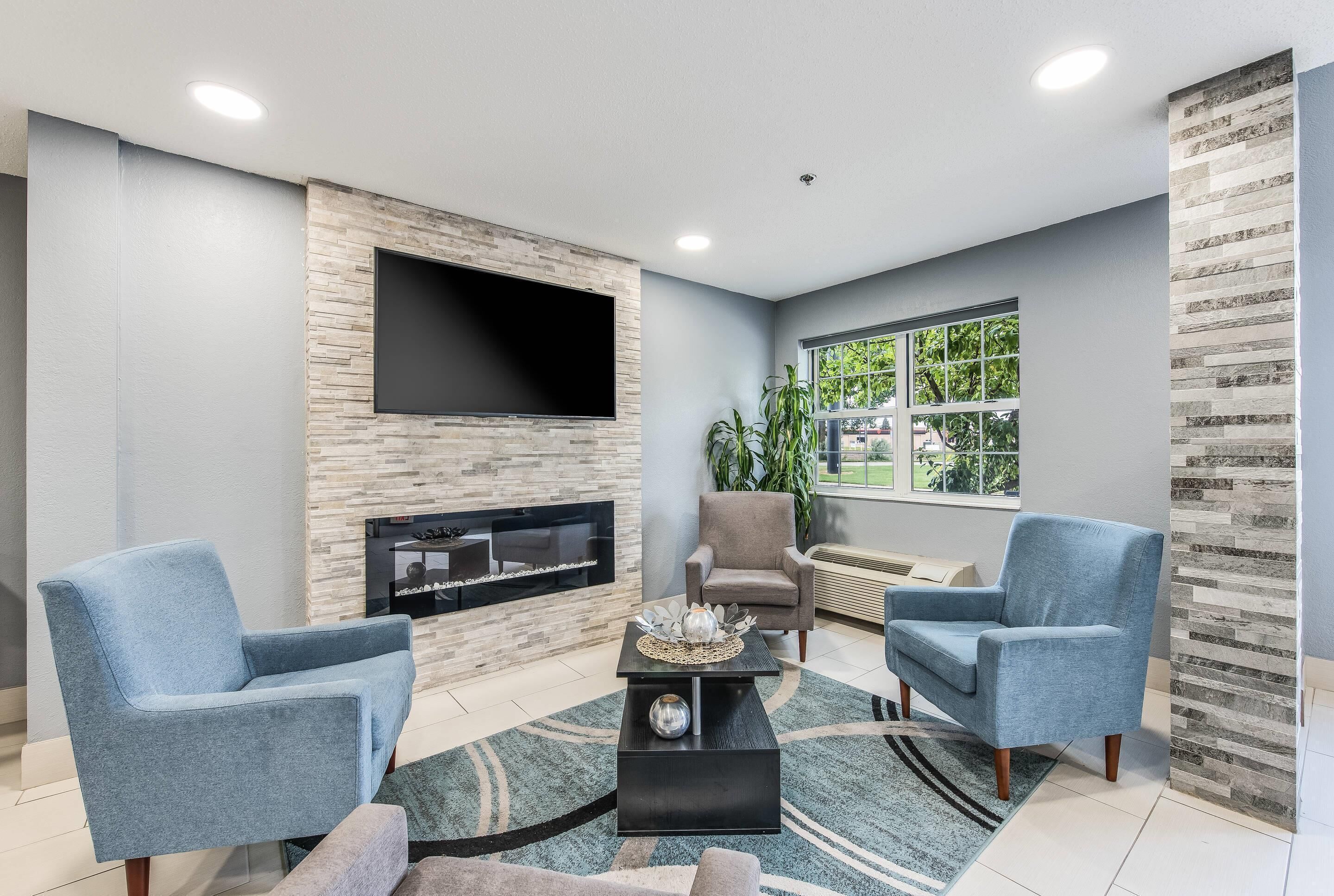 A modern living room with a flat-screen TV mounted on a stone wall, two armchairs, a coffee table, and a fireplace.