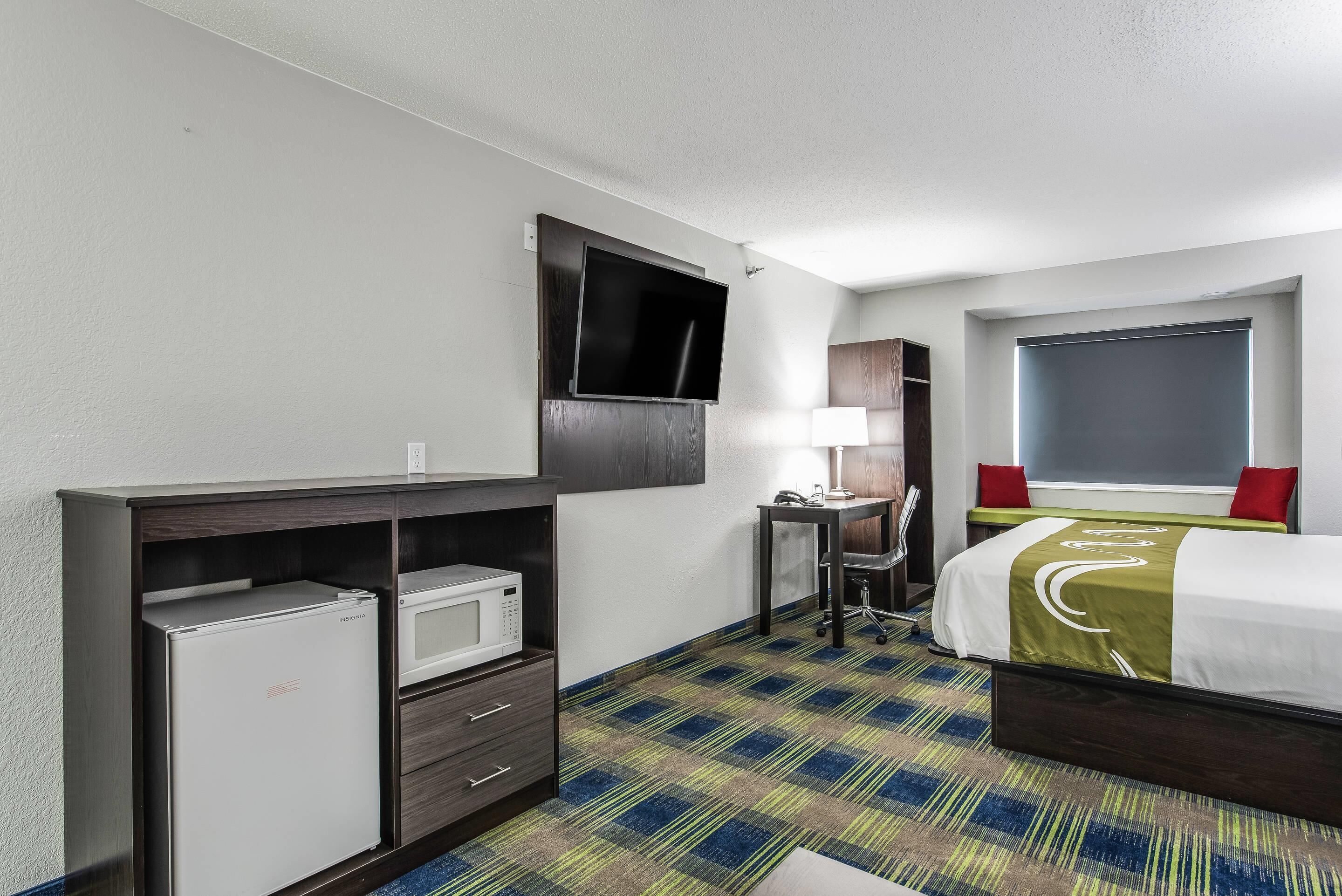 A hotel room with a bed, a desk, a television, a microwave, and a small refrigerator.