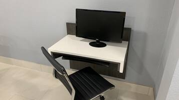 Una moderna scrivania da ufficio con un monitor del computer, una sedia da ufficio nera e un pavimento piastrellato bianco.