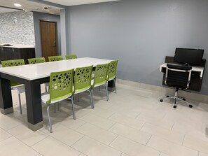 Un salón de conferencias con una mesa blanca y sillas verdes, una puerta de madera y un televisor sobre un pedestal.