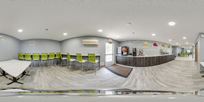 Una sala de conferencias moderna con una larga mesa y sillas verdes, un área de recepción con mostrador y una pared con diseño.