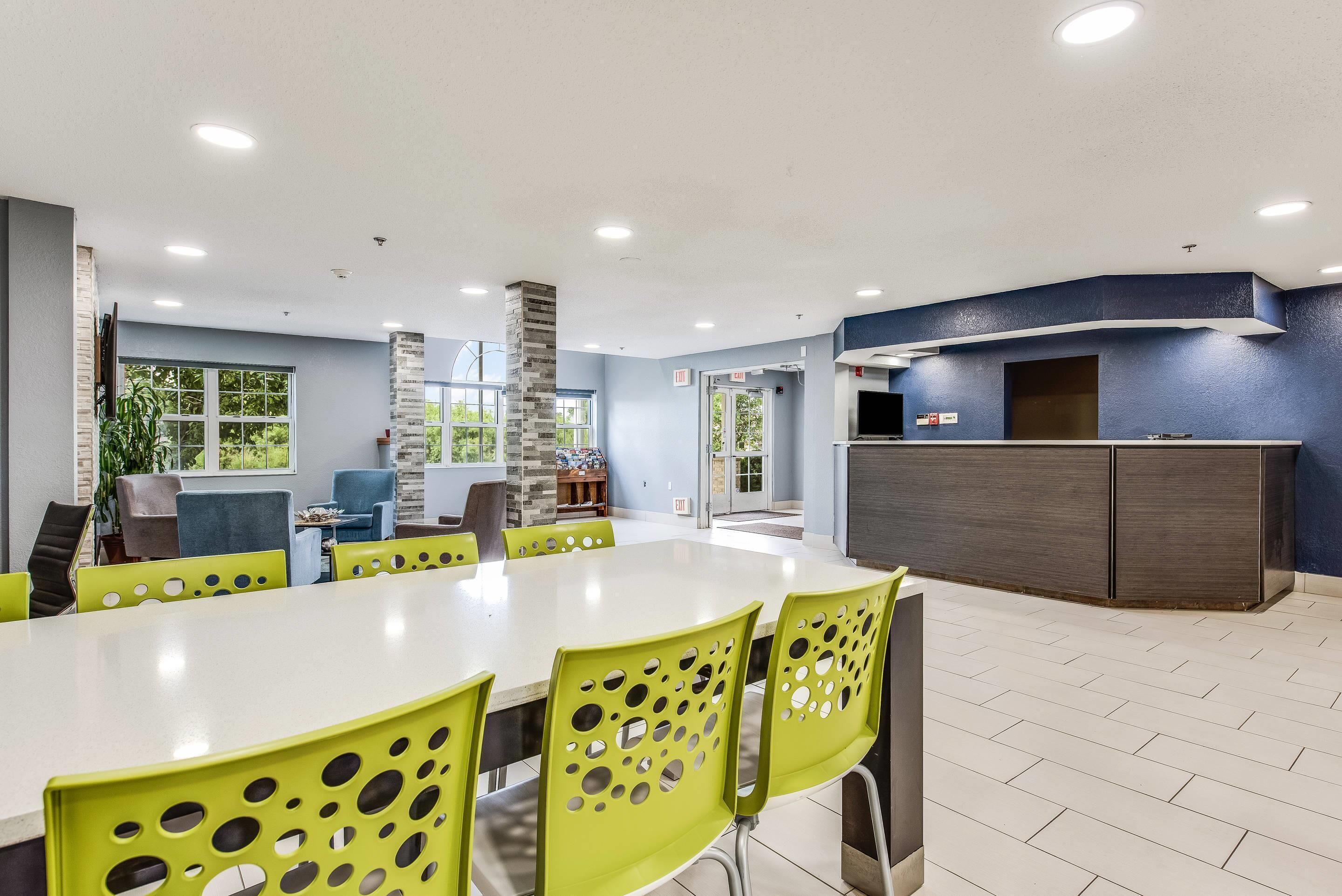 Uma área de jantar moderna com uma mesa comprida, cadeiras verdes com recortes circulares e uma parede azul de destaque.