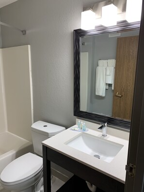 Un baño con inodoro blanco, lavamanos con espejo y zona de ducha.
