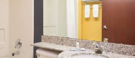 A bathroom with a white bathtub, a granite countertop sink, a mirror, and a wooden door.