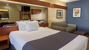A hotel room with a large bed, a desk, a chair, a television, and a framed picture on the wall.
