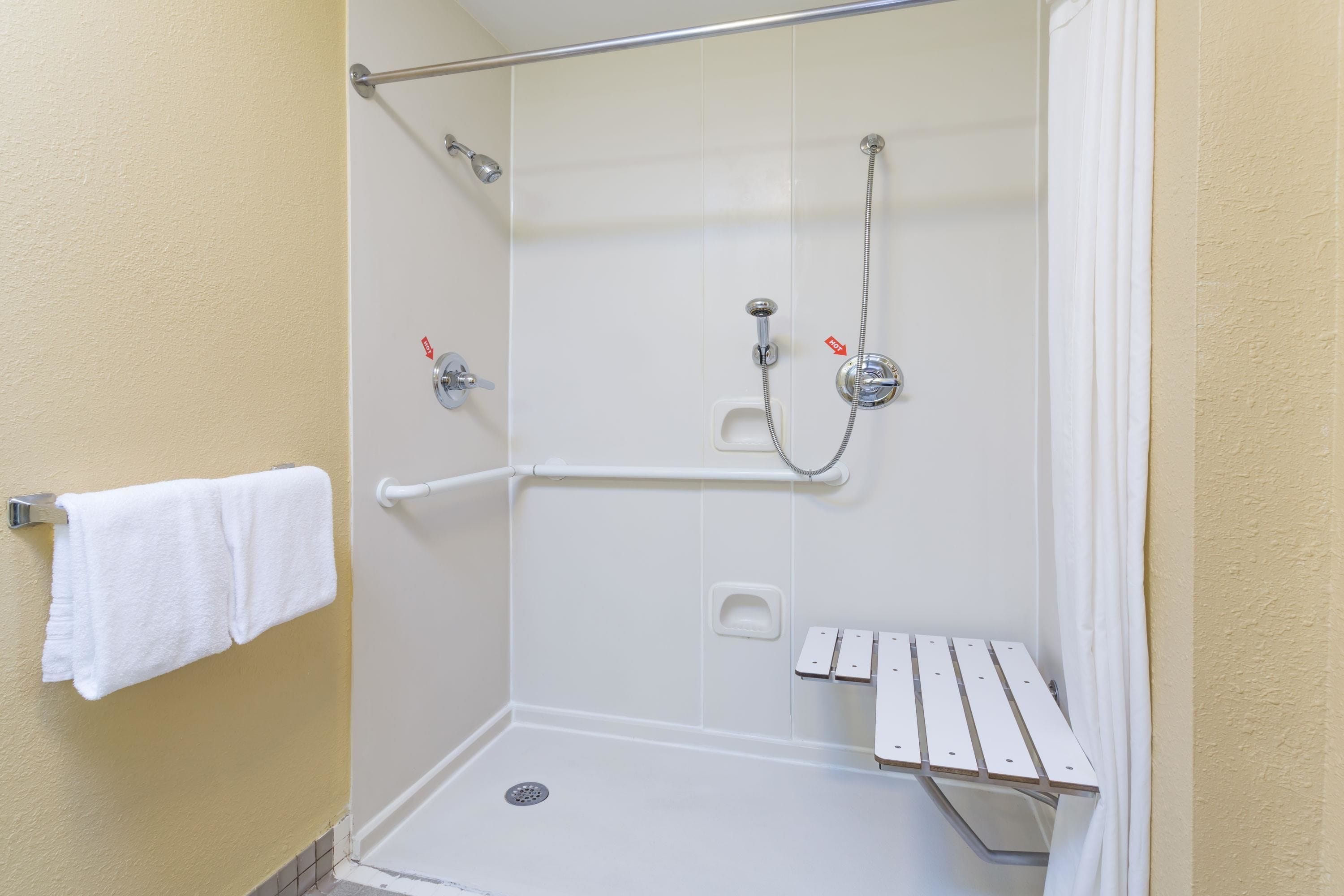 A shower with a grab bar, a towel rack, and a bench.