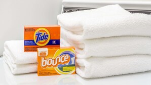 A stack of white towels and two detergent boxes labeled 'Tide' and 'Bounce'.