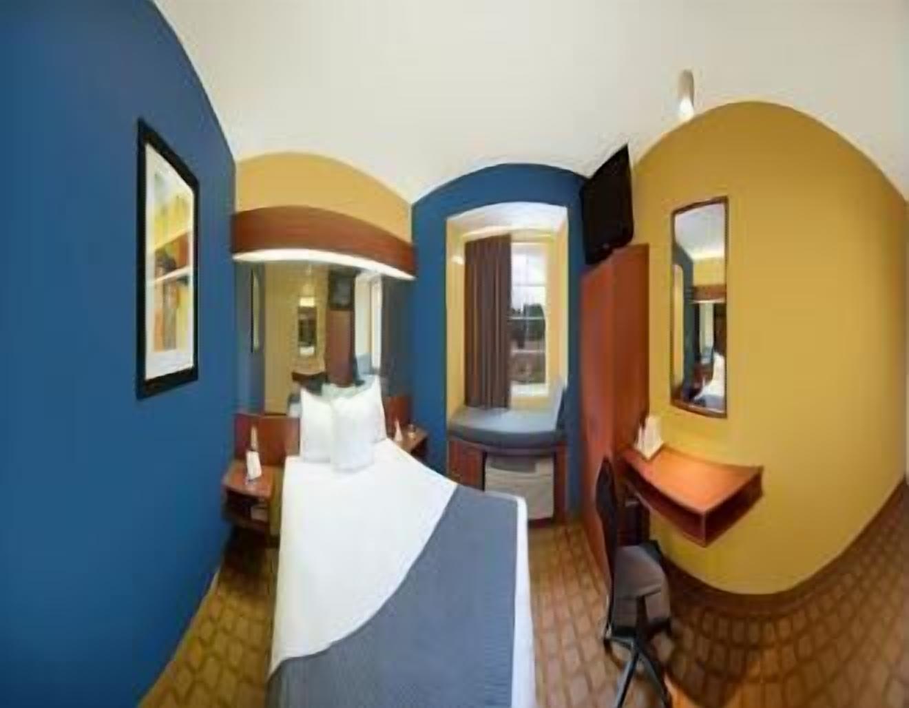 Una camera d'albergo con un letto, una scrivania, una sedia, uno specchio e una finestra.