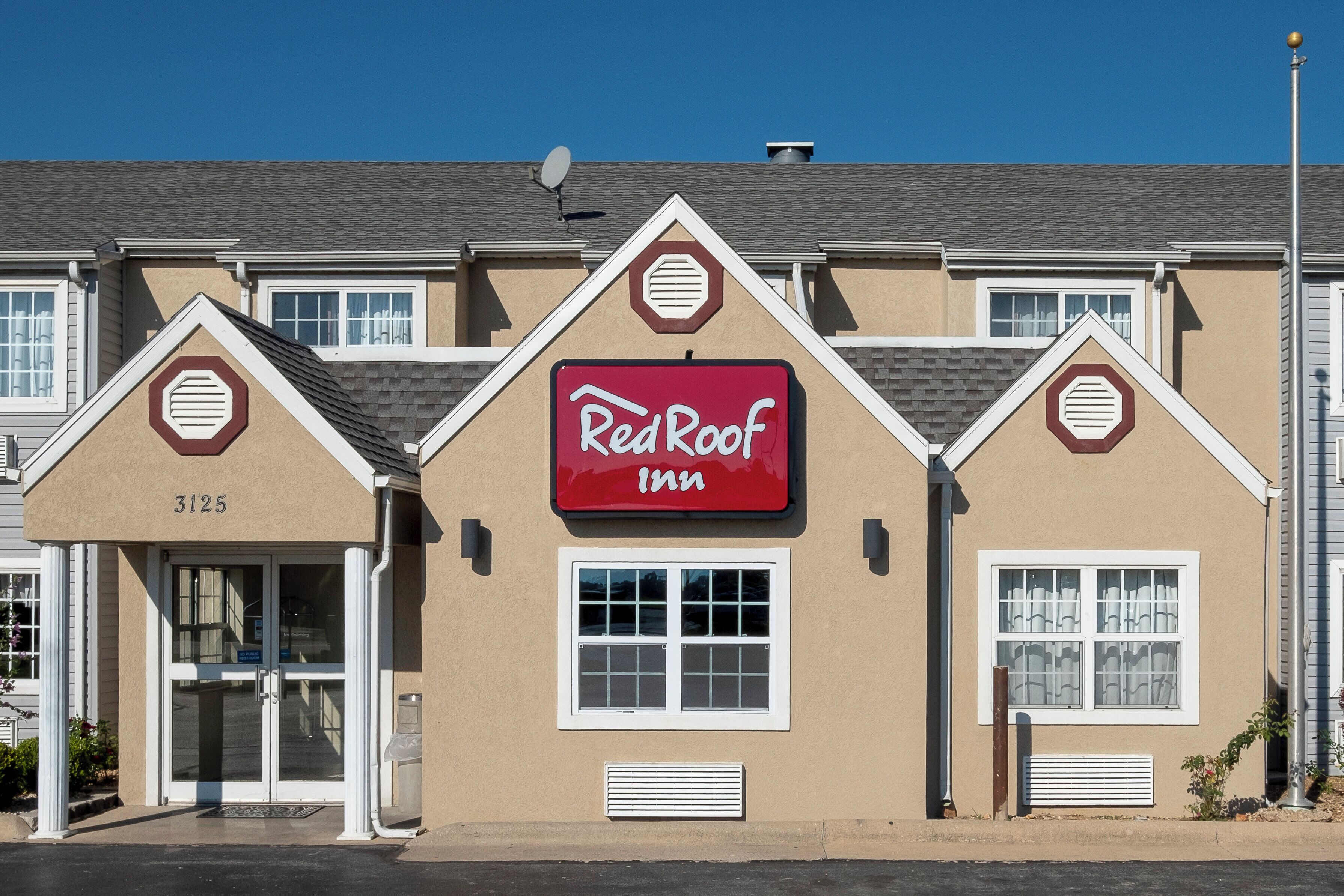 Un Red Roof Inn con un llamativo letrero rojo, el número '3125' en el edificio y una antena parabólica en el tejado.