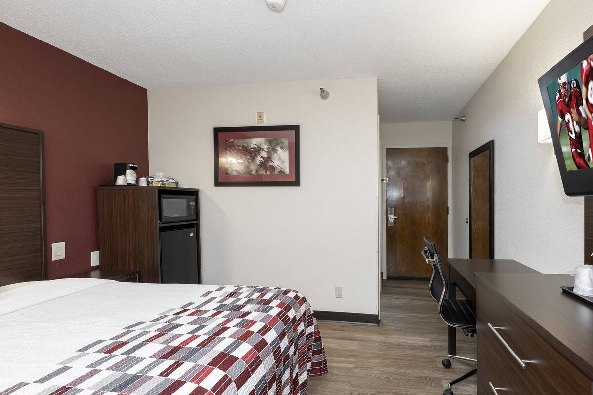 A hotel room with a bed, a desk, a chair, a microwave, and a television.