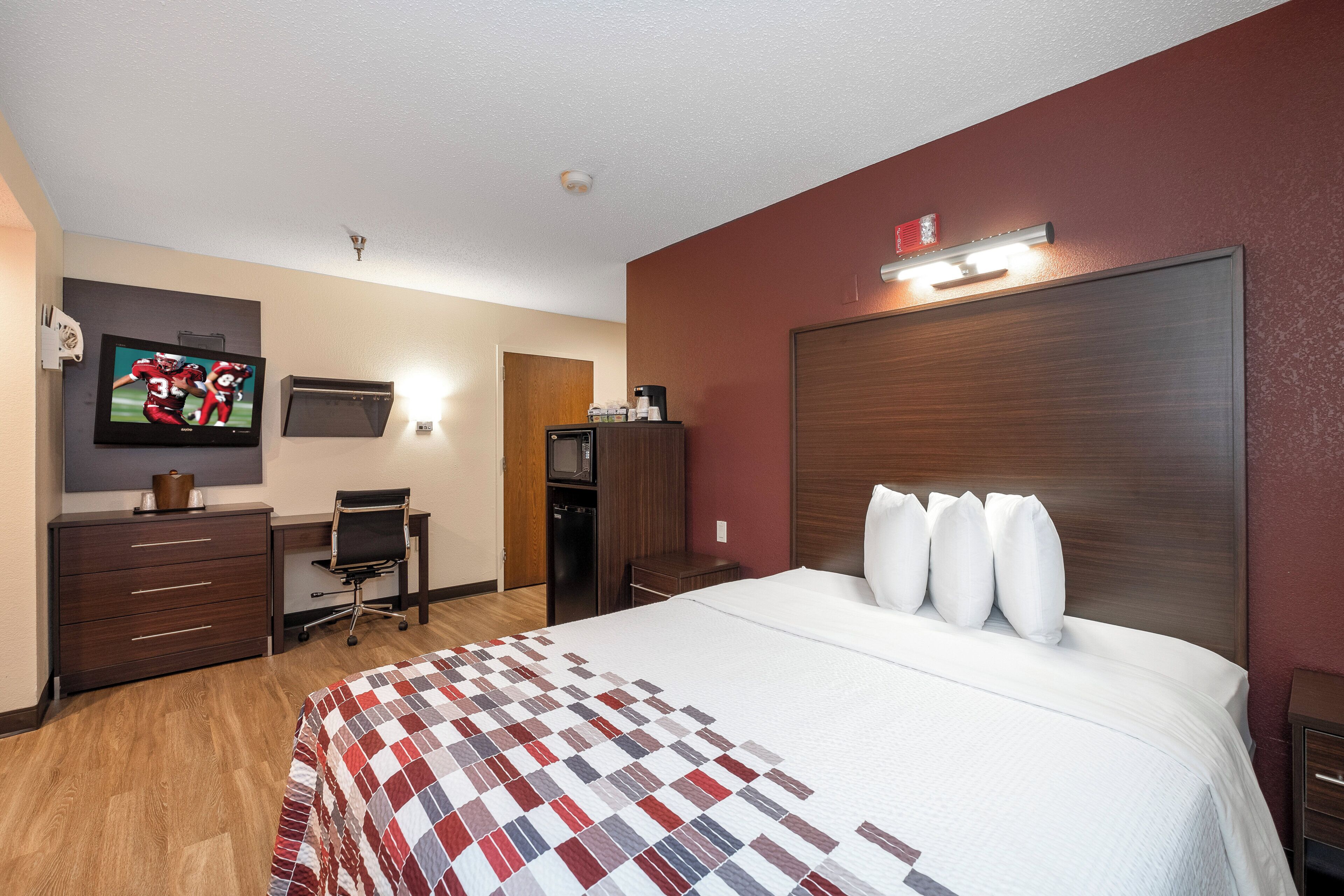 A hotel room with a bed, a desk, a television, and a microwave.