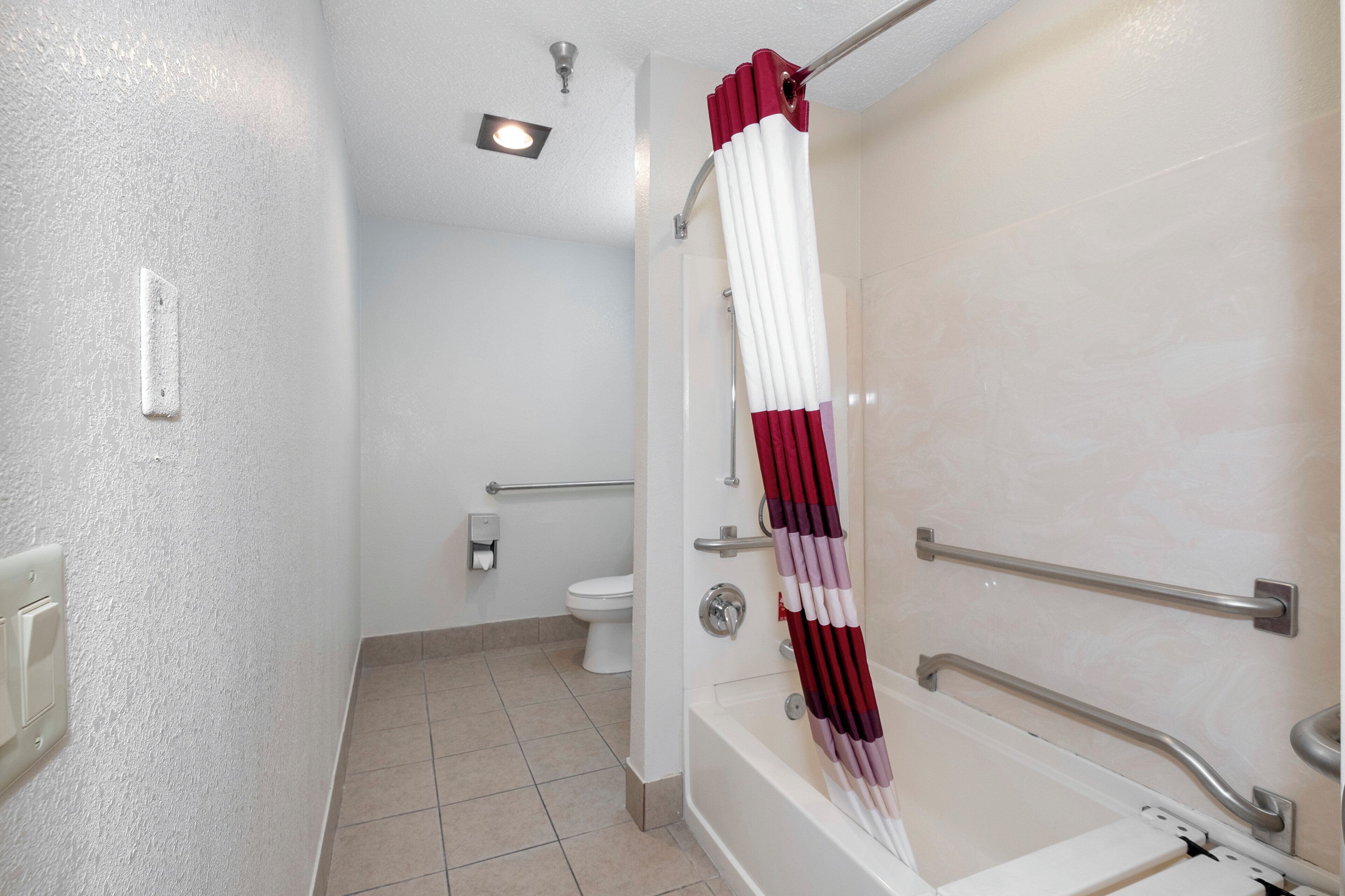 A bathroom with a shower, toilet, and handrails.