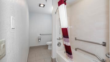 A bathroom with a shower, toilet, and handrails.