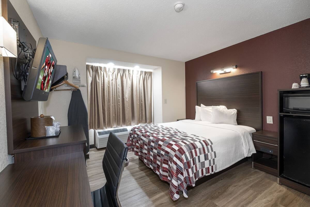 A hotel room with a bed, a desk, a chair, a TV, and a window with curtains.
