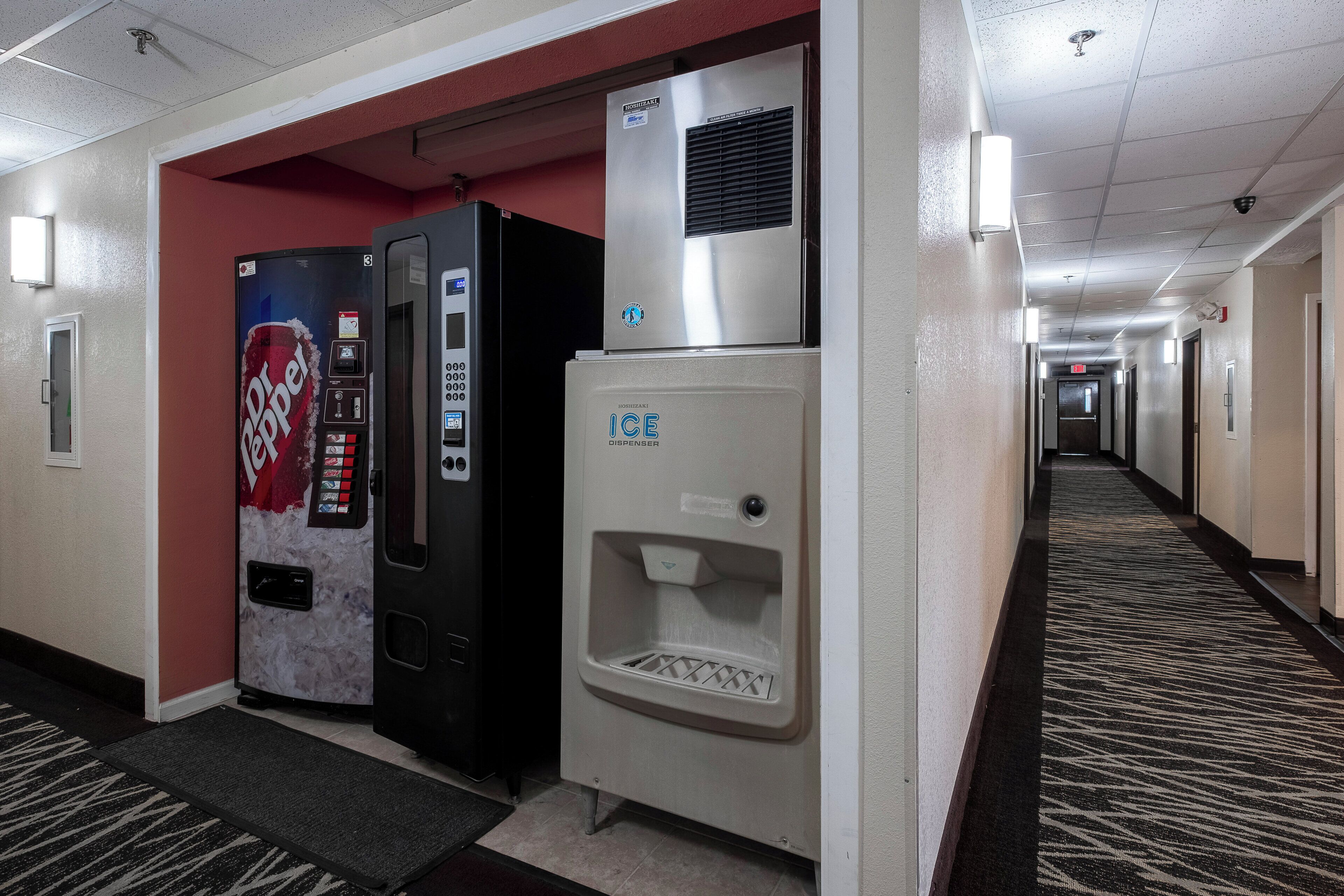 Un pasillo de hotel con máquinas expendedoras, incluyendo Dr Pepper y un dispensador de hielo.
