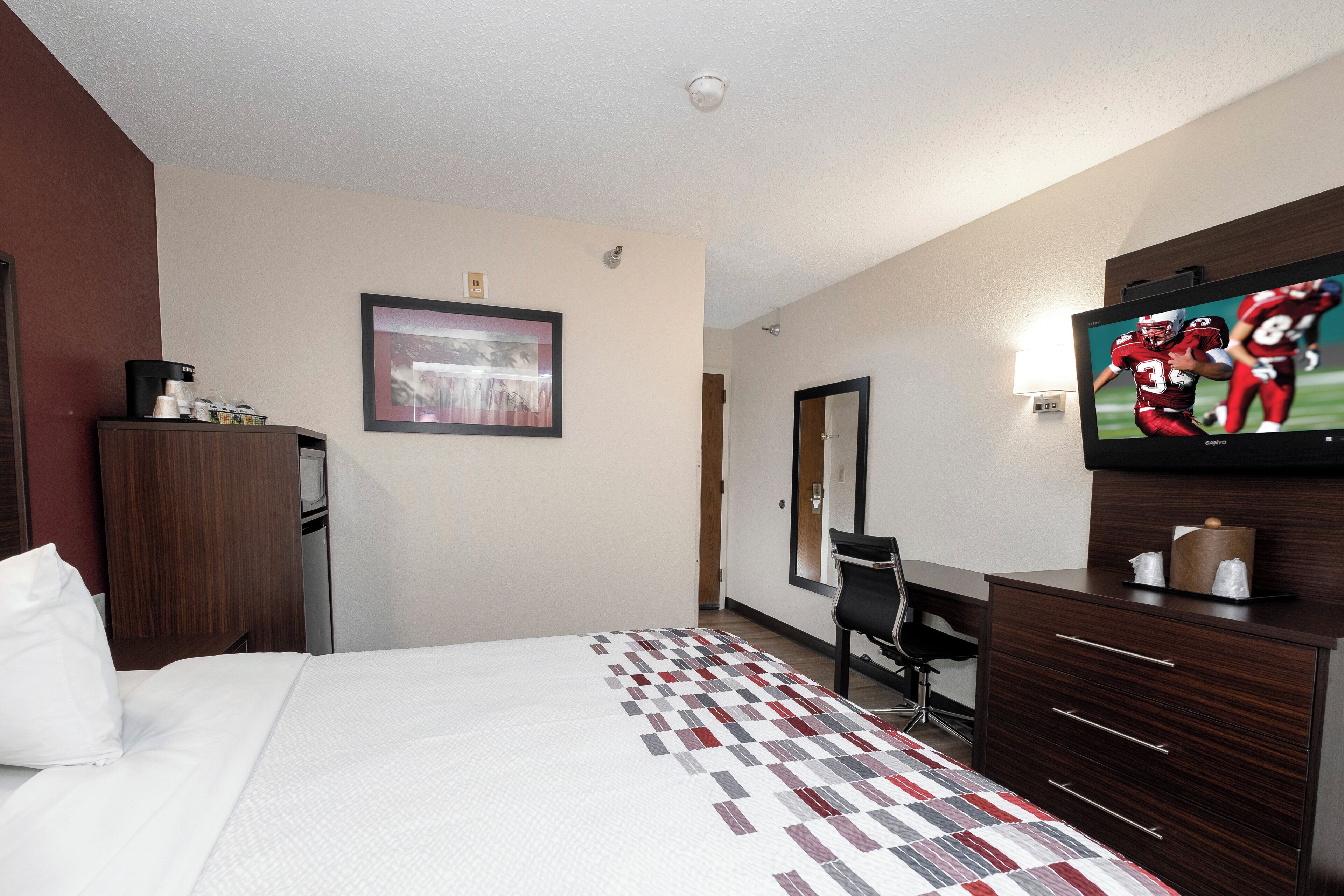 Habitación de hotel con cama, escritorio, silla, televisor y un cuadro en la pared.