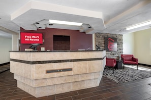 A hotel reception area with a marble counter, a red wall, a stone wall, and a Red Roof Inn sign.