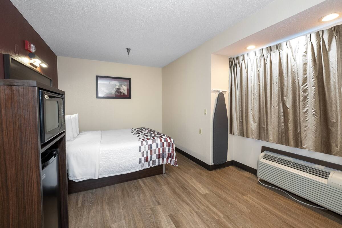 A hotel room with a bed, a television, a heater, and a window with curtains.