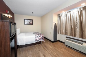 Ein Hotelzimmer mit Bett, Fernseher, einem Bild an der Wand, einem Fenster mit Vorhängen und einem Heizkörper.