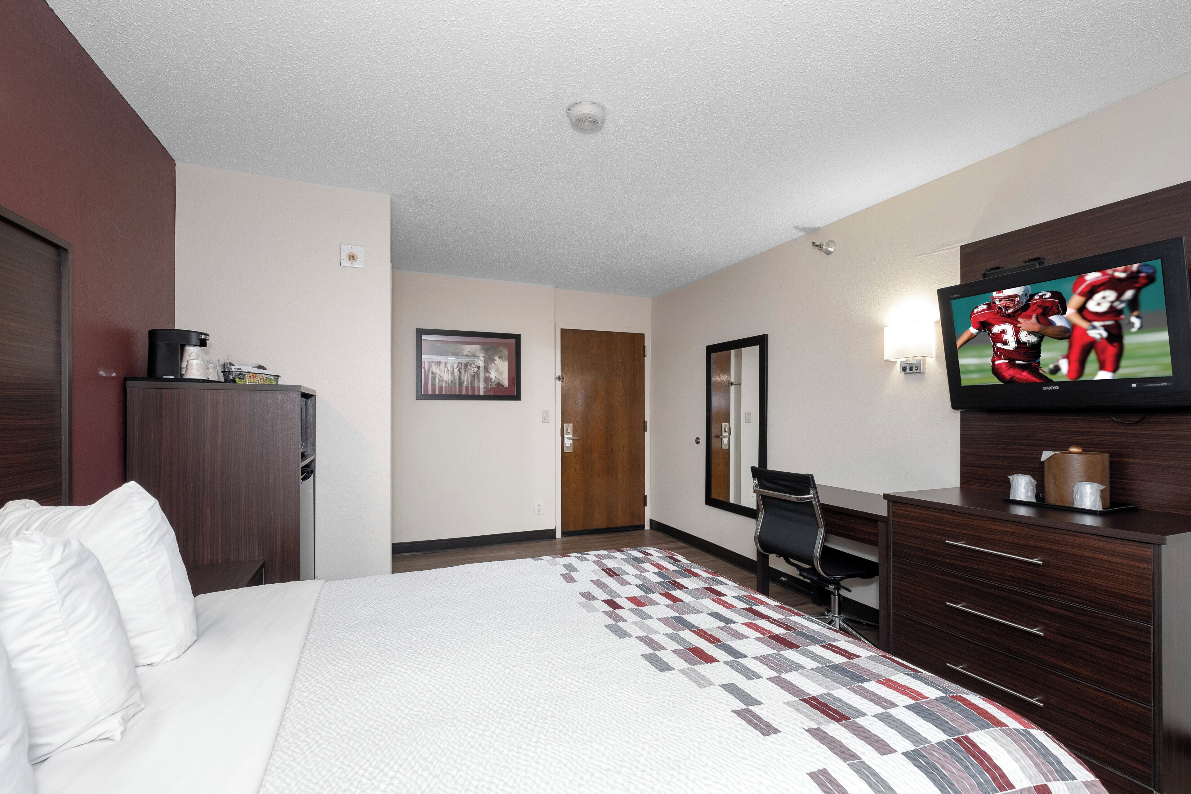 Ein Hotelzimmer mit Bett, Schreibtisch, Stuhl, Fernseher und einer Tür.