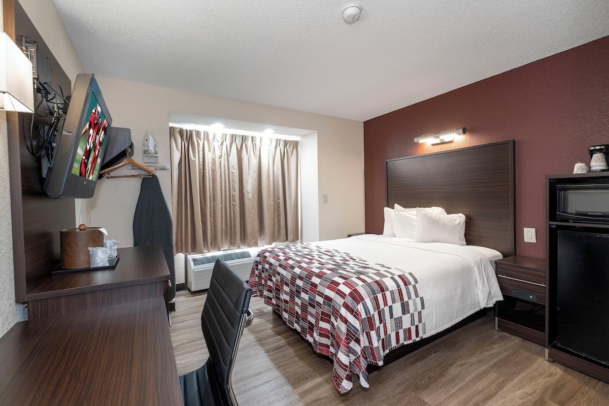 A hotel room with a bed, bedside table, TV, and a window with curtains.