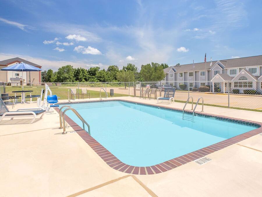 A rectangular swimming pool with a brick border, surrounded by a fence, and a building with a blue roof in the background.