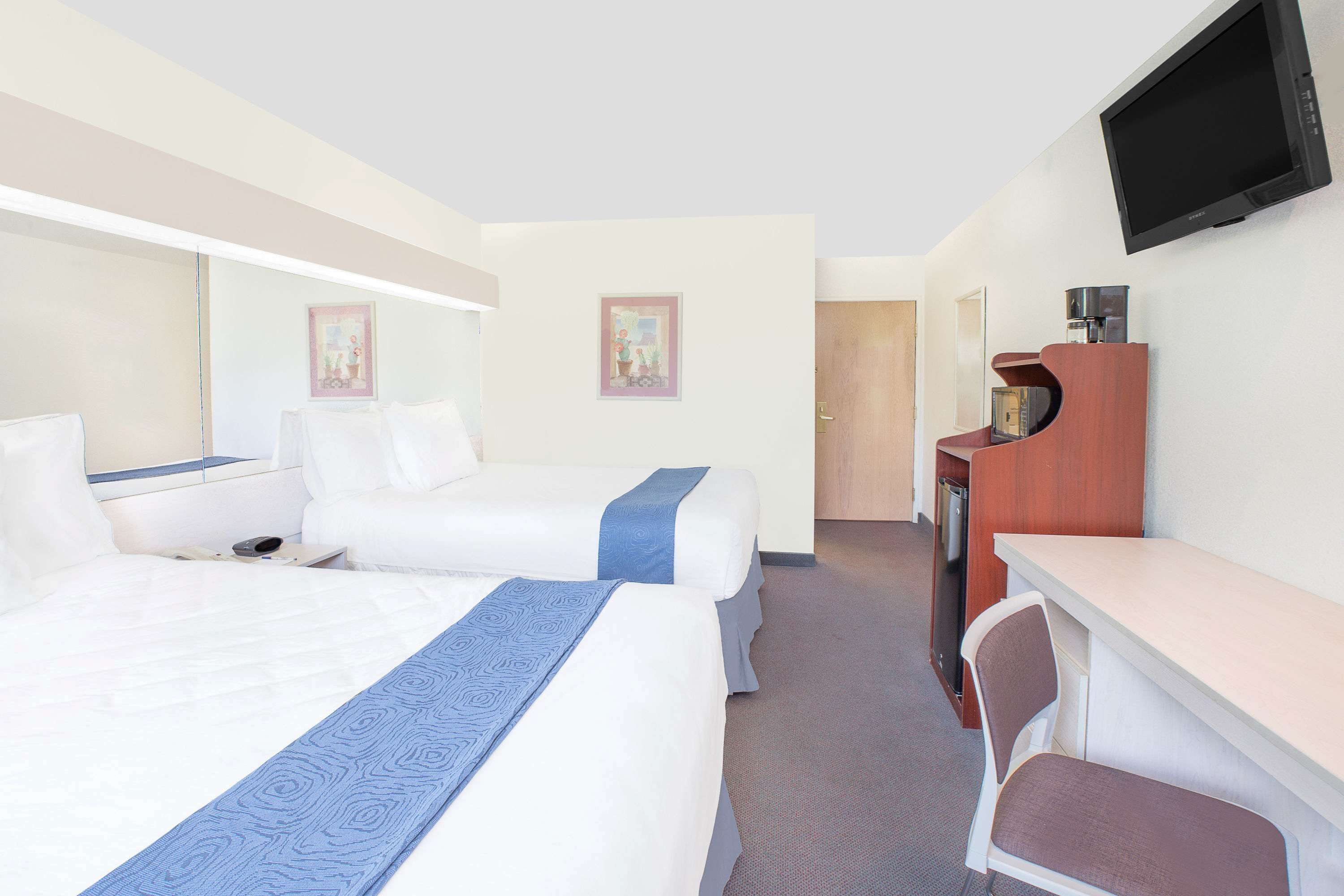 A hotel room with two beds, a desk, a chair, a television, and a door leading to a bathroom.