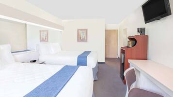 A hotel room with two beds, a desk, a chair, a television, and a door leading to a bathroom.