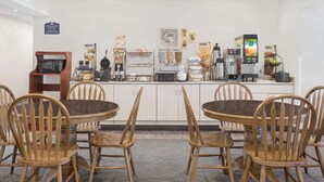 Una barra de desayuno con sillas de madera, un microondas, máquinas de café y diversos alimentos.