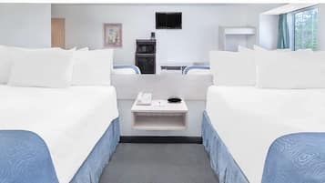 Habitación de hotel con dos camas, un escritorio pequeño con un teléfono y un tazón, un microondas, un televisor y una ventana con vista a árboles.