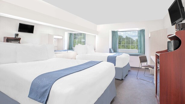 Una habitación de hotel con dos camas, un escritorio, una silla, un televisor y una ventana con cortinas.